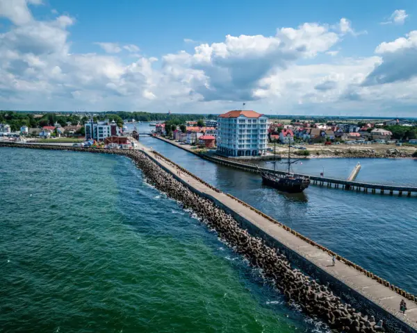 Widok na port w Darłówku Zachodnim z falochronem, budynkiem i statkiem pirackim.