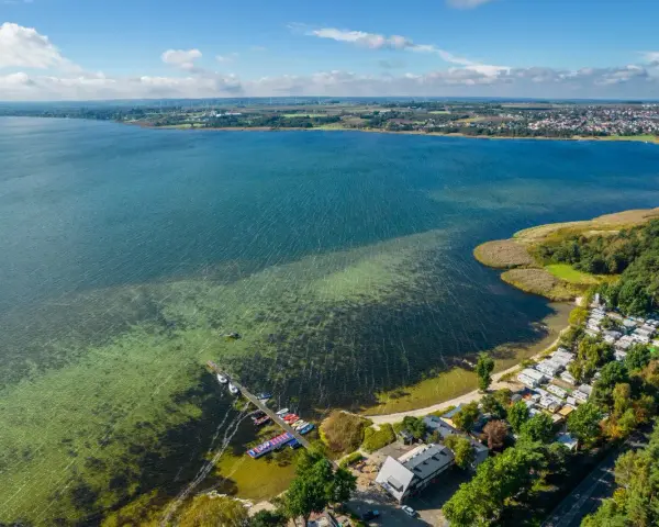 Malowniczy cypel na Helu z kempingiem, pomostem i kolorowymi łódkami. W oddali widać miasto i farmę wiatraków.