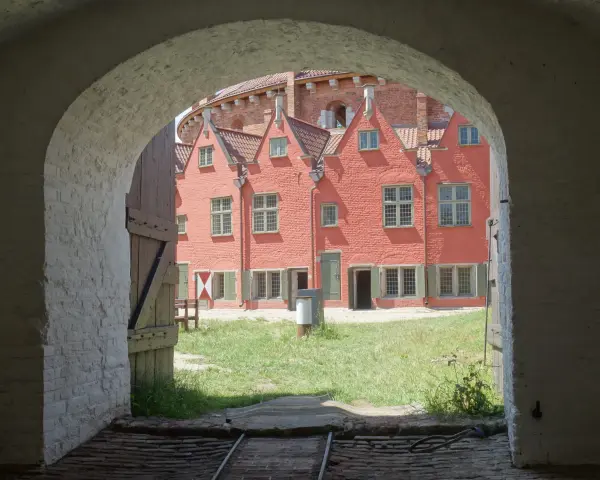 Przez łuk widać dziedziniec twierdzy Wisłoujście z ceglanymi budynkami i zieloną trawą.