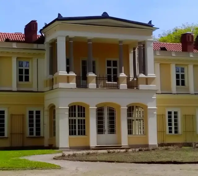 Muzeum tradycji szlacheckiej w Waplewie Wielkim. Żółty dwór z kolumnowym portykiem i czerwonym dachem.