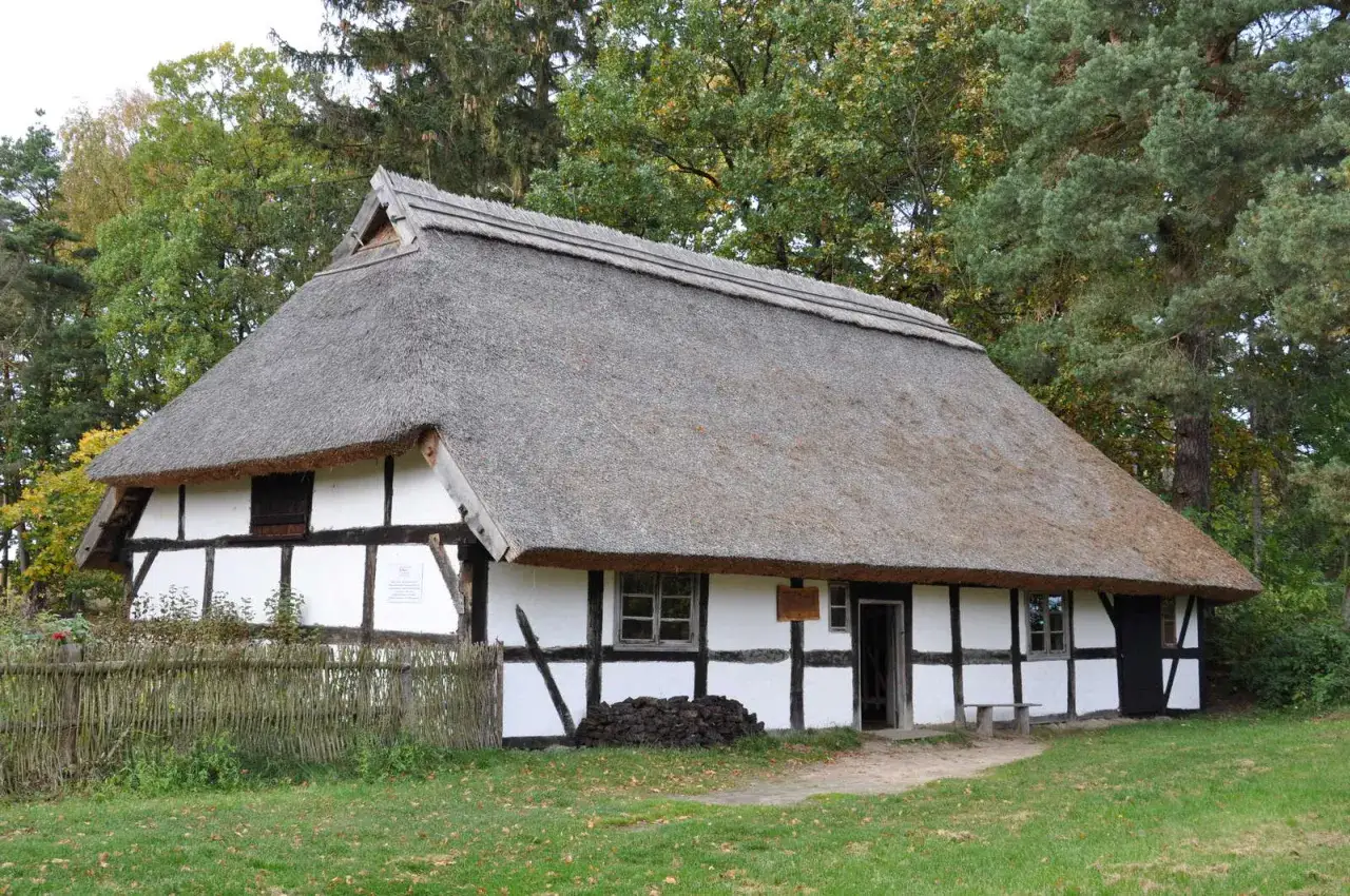 Muzeum Wsi Słowińskiej w Klukach: tradycyjny dom z bielonymi ścianami i strzechą, otoczony zielenią.