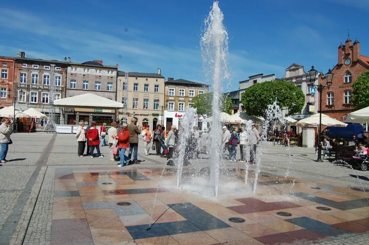 Tętniący życiem rynek w Kościerzynie z fontanną i ludźmi spacerującymi pośród kolorowych kamieni. To świetne kościerzyna atrakcje.