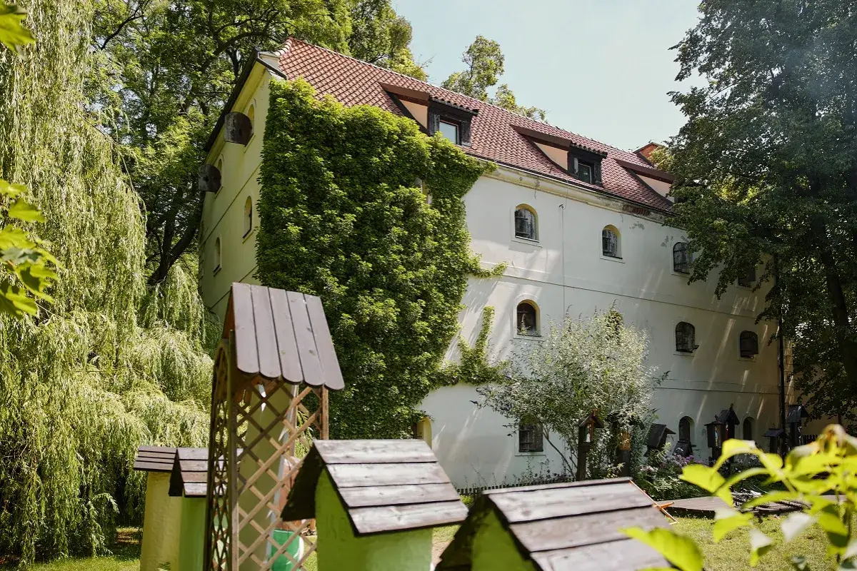 Oddział etnografii - spichlerz opacki, otoczony zielenią, z widocznymi pszczelimi ulami w ogrodzie.