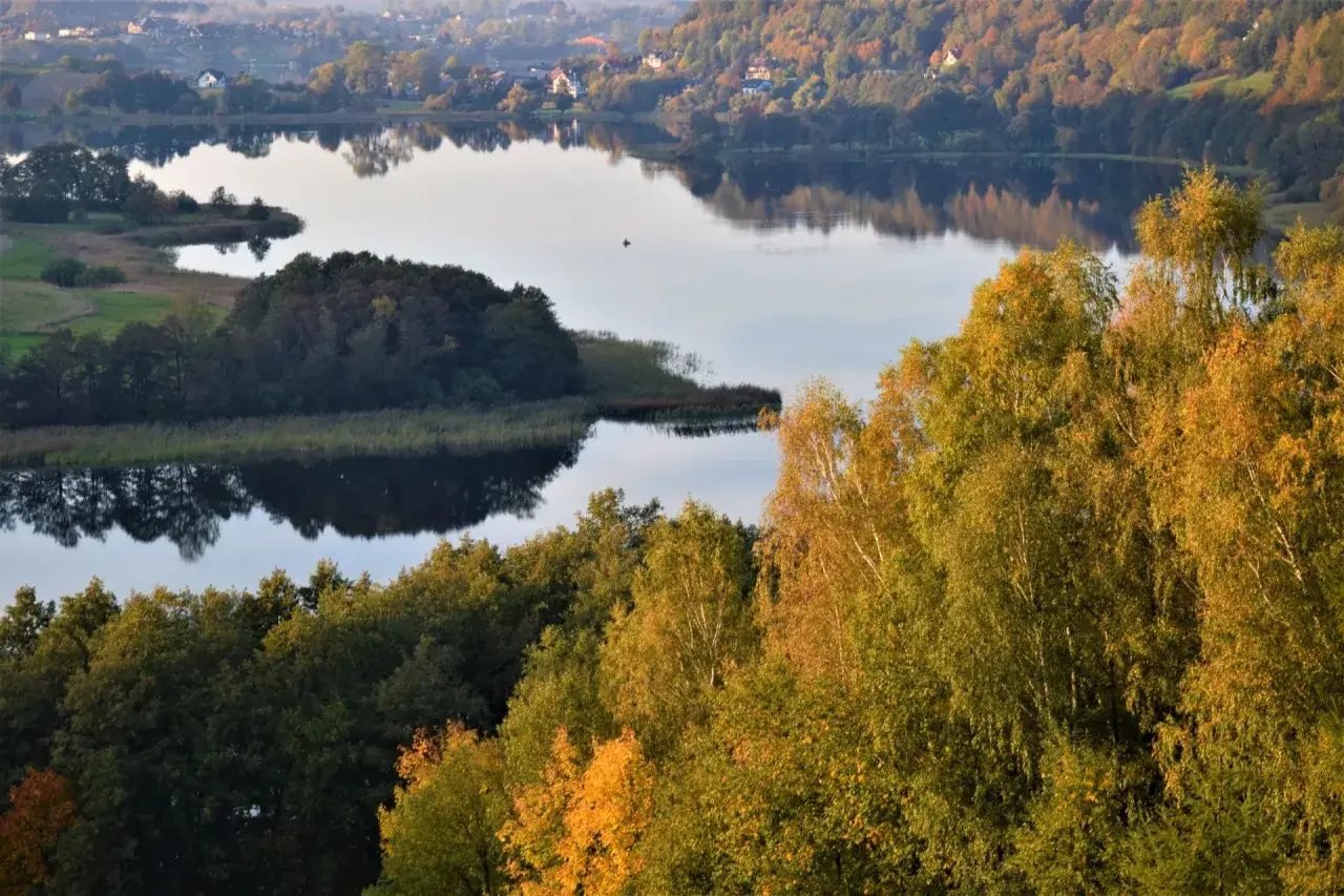 Złota jesień na Kaszubach. Jezioro odbija jesienne barwy lasów, a na wodzie widać samotną łódkę.