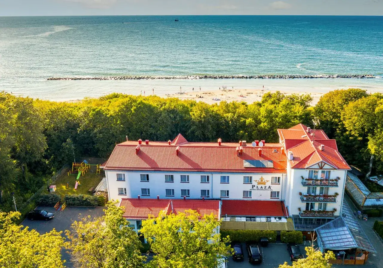 Hotel Plaza w Darłówku, tuż przy plaży. Widać morze, piasek, drzewa i plac zabaw.