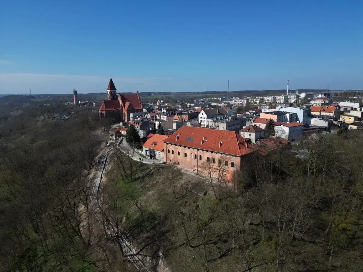 Widok na miasto z czerwonymi dachami, kościołem i zamkiem. W dole strome schody prowadzące przez las. Nowe nad Wisłą.