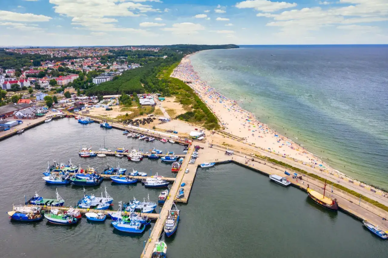 Władysławowo miasto tętni życiem: port pełen łodzi, plaża z tłumem turystów i morze.