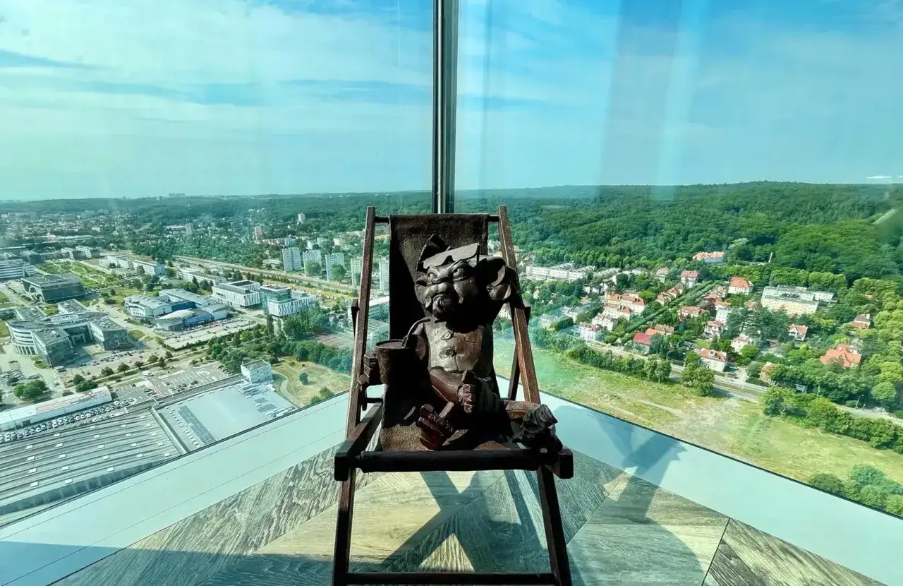 Figurka lew hewelion na leżaku, z widokiem na miasto i las.
