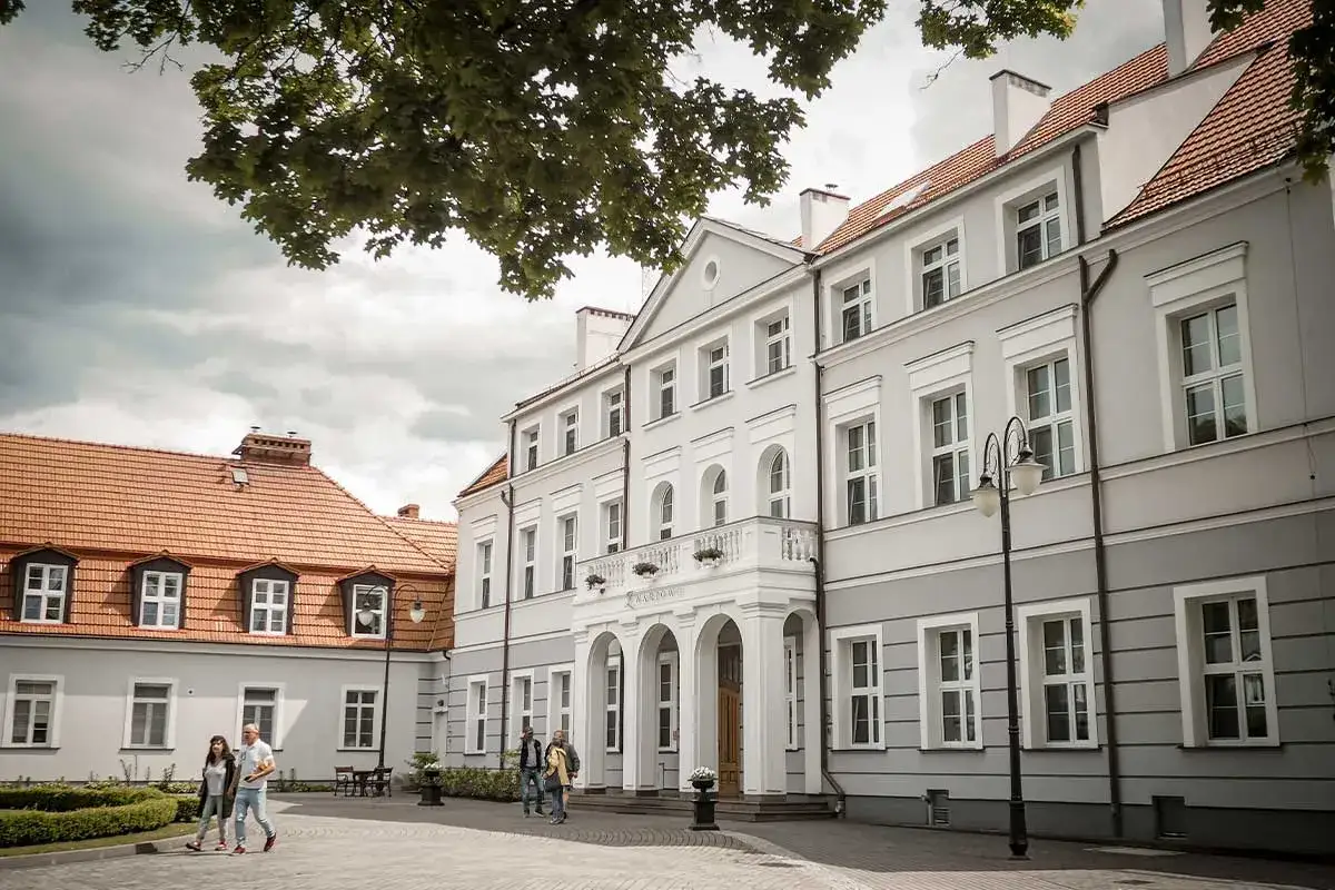 Elegancki, szary budynek z białymi zdobieniami i łukowym wejściem. Na fasadzie widnieje napis