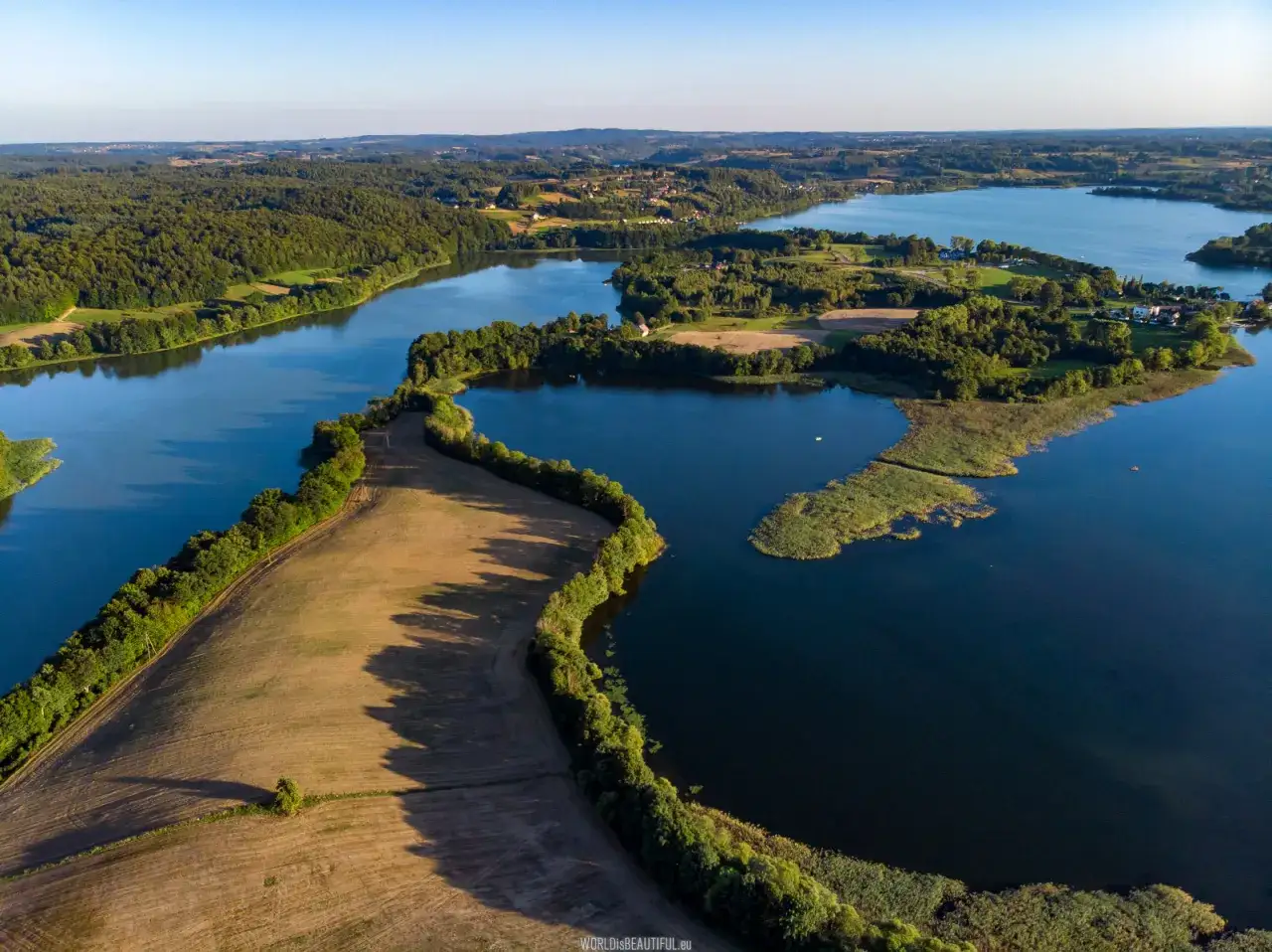 Malownicze jeziora i lasy tworzą krajobraz jak ze Szwajcarii Kaszubskiej. Pola uprawne i zarośla nad wodą.