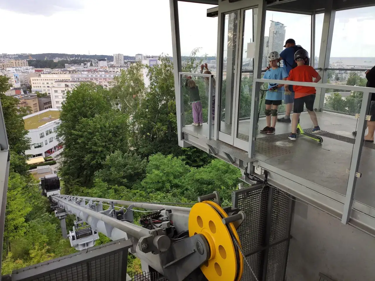Dzieci na hulajnogach czekają na wjazd kolejką na kamienną górę w Gdyni. Widok na miasto i morze.