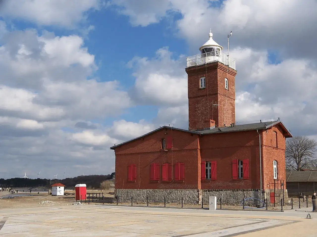 Ceglana latarnia morska i budynki w Darłówku, w tle wiatraki i plaża. Jedna z atrakcji nad Bałtykiem.