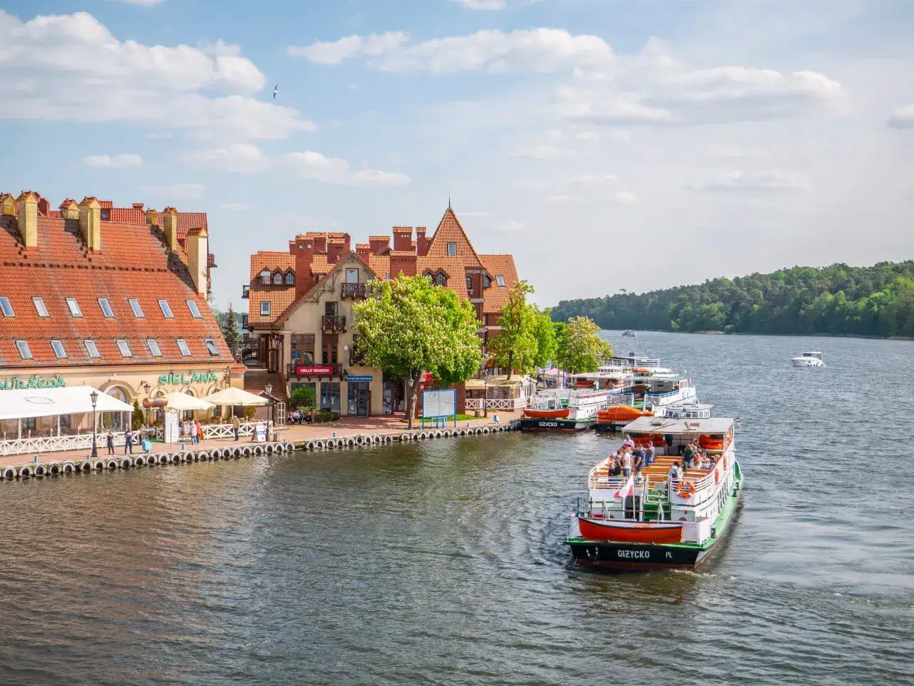 Port w Mikołajkach z cumującymi statkami i kamieniczkami. Idealne miejsce na rejs i podziwianie atrakcji Mazur.