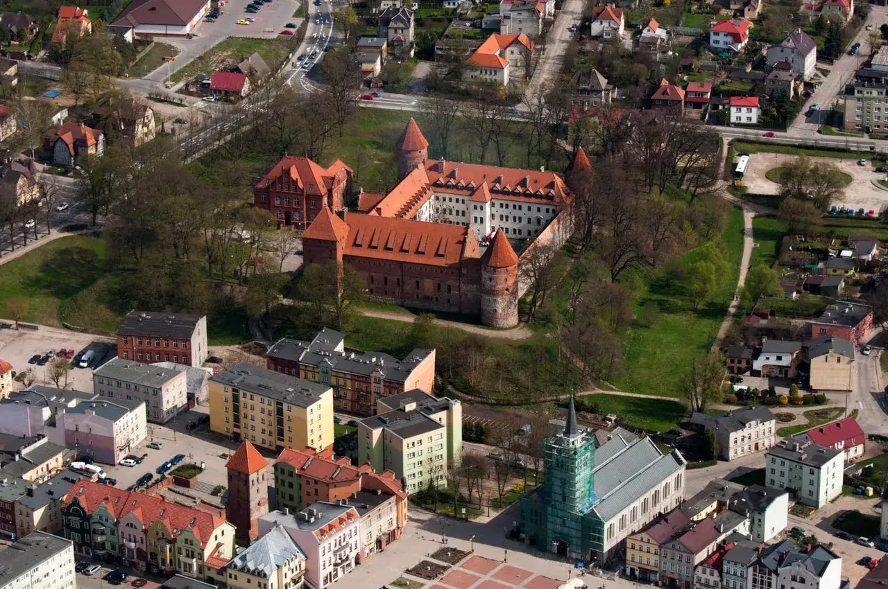 Zamek w Bytowie z czerwonej cegły, otoczony zielenią i zabudowaniami miejskimi, prezentuje się majestatycznie z lotu ptaka.