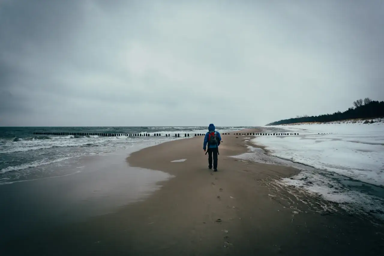 Spacer po plaży na Helu poza sezonem. W oddali widać las i zamarznięte fragmenty morza.