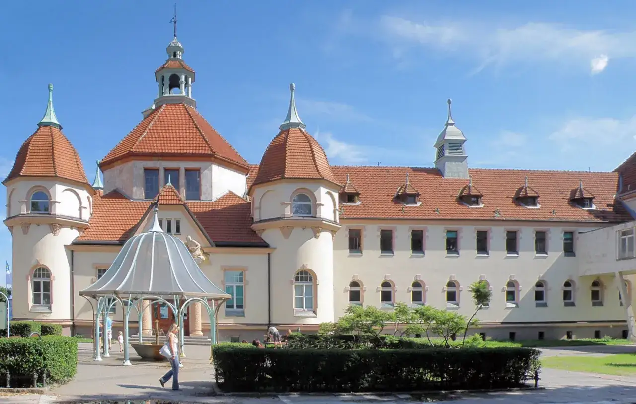 Elegancki zakład balneologiczny Sopot z charakterystycznymi wieżyczkami i czerwonym dachem, otoczony zielenią.